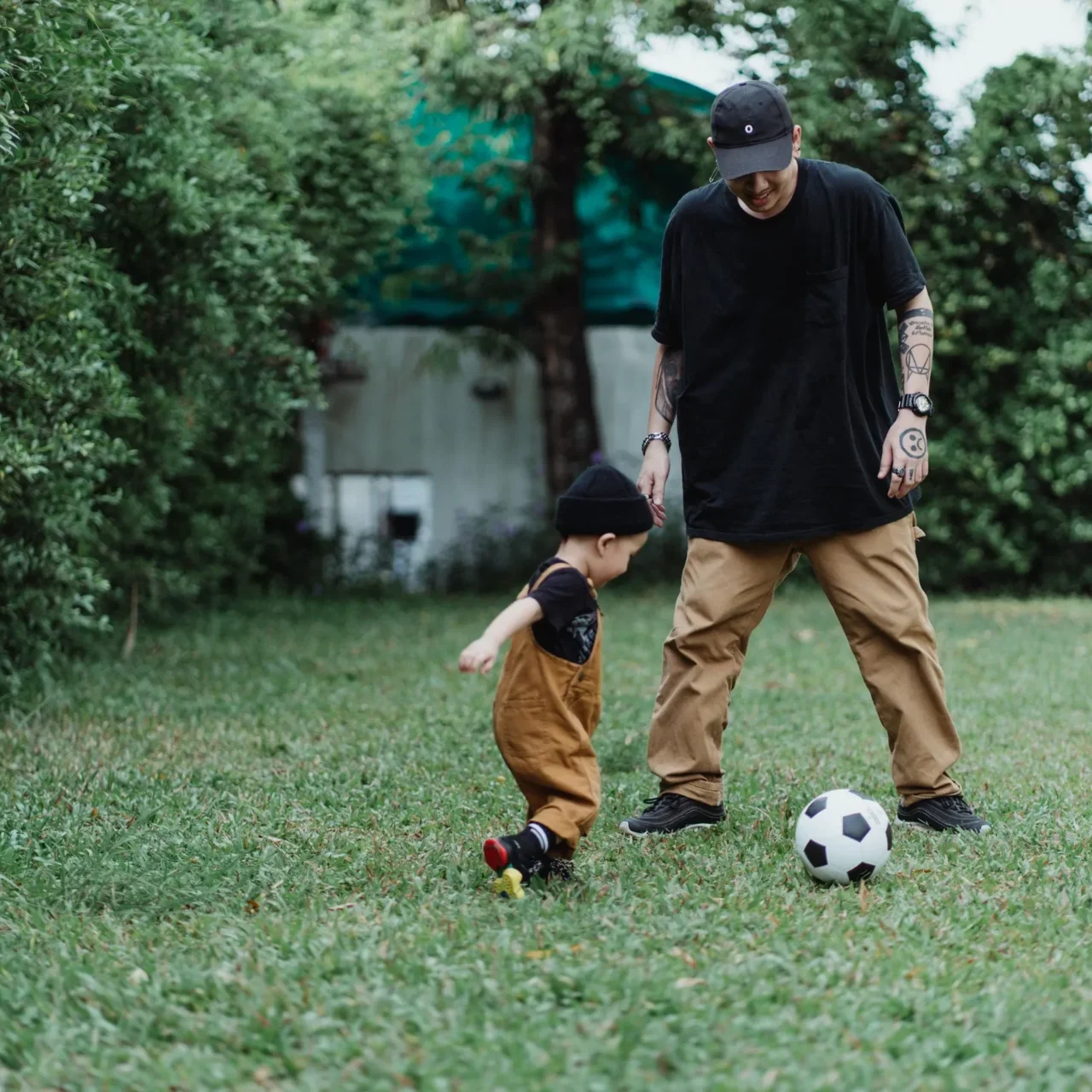 A man and child playing soccer in the grass.